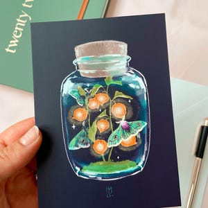Illustrated postcard of a glass jar. Three emperor moths are drawn to the light of the little Chinese Lanterns. 
Dreamy cottagecore illustration inspired by the falling darkness of autumn evenings.
The photo also shows an envelope that is included.