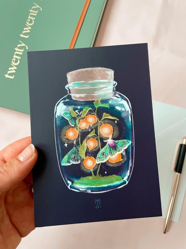 Illustrated postcard of a glass jar. Three emperor moths are drawn to the light of the little Chinese Lanterns. 
Dreamy cottagecore illustration inspired by the falling darkness of autumn evenings.
The photo also shows an envelope that is included.