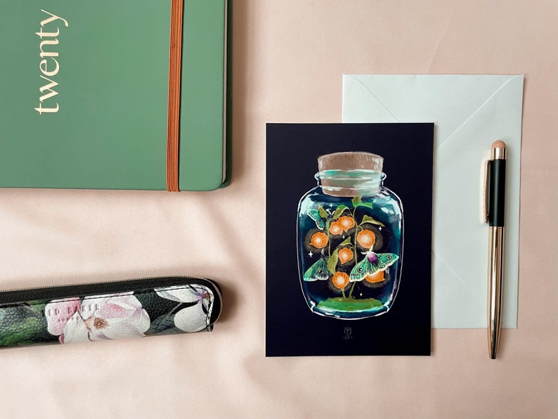 Illustrated postcard of a glass jar. Three emperor moths are drawn to the light of the little Chinese Lanterns. 
Dreamy cottagecore illustration inspired by the falling darkness of autumn evenings.
The photo also shows an envelope that is included.