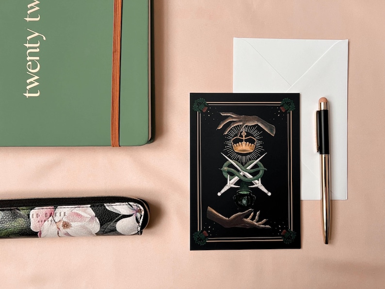 Illustrated Macbeth postcard
picturing witchy hands, golden crown, a snake wrapped around two daggers, and a couldron. There is a thistle in each corner, and two golden lines decorating all 4 sides of the card.

Comes with a white envelope.