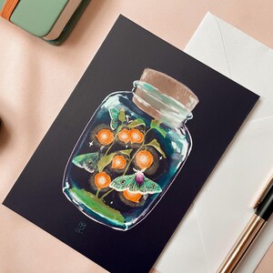 Illustrated postcard of a glass jar. Three emperor moths are drawn to the light of the little Chinese Lanterns. 
Dreamy cottagecore illustration inspired by the falling darkness of autumn evenings.
The photo also shows an envelope that is included.