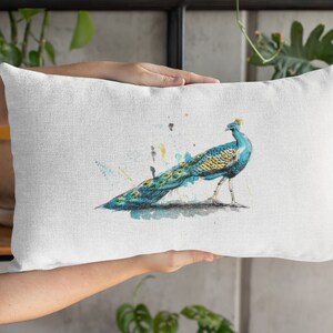 May include: A white linen pillow with a watercolor illustration of a peacock with a blue and green tail. The peacock is standing on a branch with a yellow and green background.