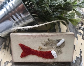 May include: A wooden sign with a mermaid design. The mermaid is made of white and red glitter and has a gold star on her tail. The sign has a twine hanger.