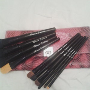 May include: Set of black makeup brushes with a pink snakeskin-patterned case. The brushes have the name "Dana Sutton" printed on them.