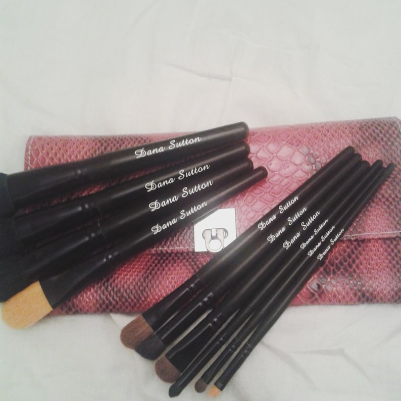 May include: Set of black makeup brushes with a pink snakeskin-patterned case. The brushes have the name "Dana Sutton" printed on them.