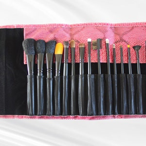 May include: A pink makeup brush roll with black mesh pockets holds a set of 17 makeup brushes with black handles. The brushes have different shapes and sizes for applying various makeup products.