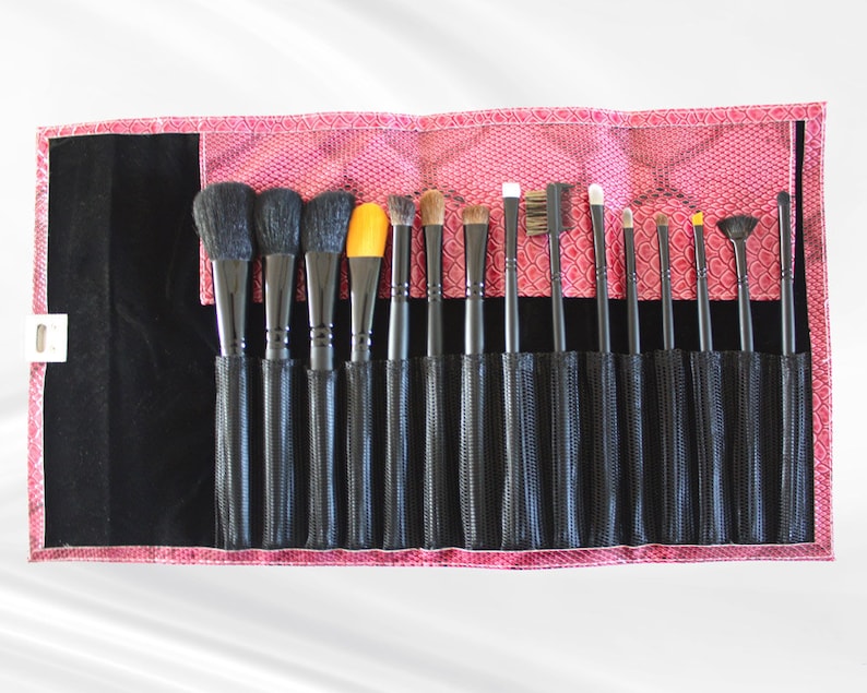 May include: A pink makeup brush roll with black mesh pockets holds a set of 17 makeup brushes with black handles. The brushes have different shapes and sizes for applying various makeup products.