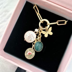 Puede incluir: Un collar de cadena de oro con un dije que presenta una perla, una piedra preciosa verde, un dije de mariposa y un dije redondo con un diseño floral.