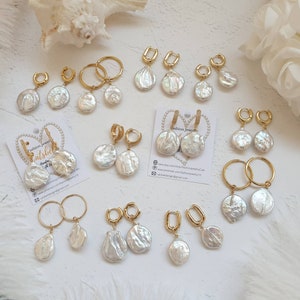 Op de afbeelding: Een verzameling gouden creolen met parelhangers. De oorbellen zijn gerangschikt op een wit oppervlak met een hartvormige kaart met de tekst "Fashion Jewelry" en website-informatie.