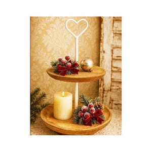 Könnte beinhalten: Ein zweistufiges Serviertablett aus Holz mit einem weißen herzförmigen Griff. Die obere Ebene enthält eine dekorative Anordnung mit roten Beeren und einer Schleife sowie einen goldenen Ornament. Die untere Ebene hat eine brennende Kerze und eine ähnliche Anordnung.