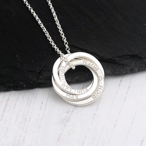 May include: Silver necklace with a pendant featuring four interlocking rings with the names "Max", "Belinda", "Richard", and "Maria" engraved on them.