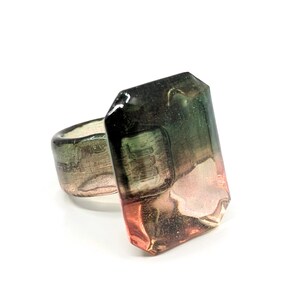 May include: A ring with a large, faceted, green and pink gemstone. The gemstone is set in a silver band.