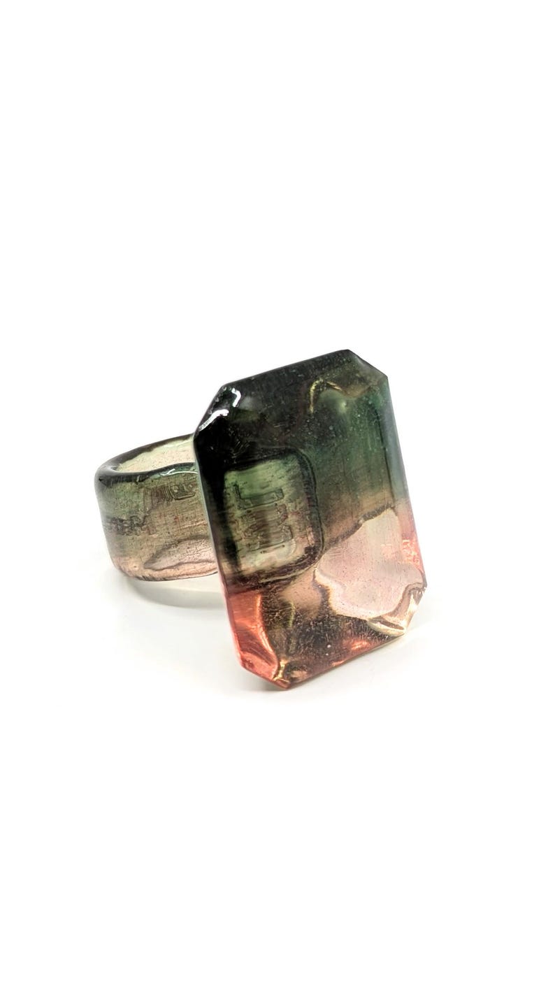 May include: A ring with a large, faceted, green and pink gemstone. The gemstone is set in a silver band.