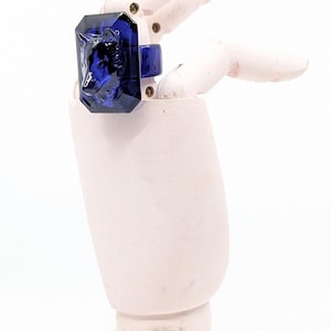 Könnte beinhalten: Ein dunkelblauer Glasring mit facettiertem Design. Der Ring befindet sich an einem hölzernen Handmodell.