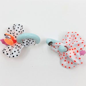 May include: A pair of earrings with a white and black polka dot design and a light blue hoop. One earring has a pink and orange flower accent, while the other has a red and white polka dot design.