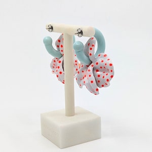 May include: A pair of hoop earrings with a white and red polka dot design. The earrings are made of a light blue material and have a silver hook closure.