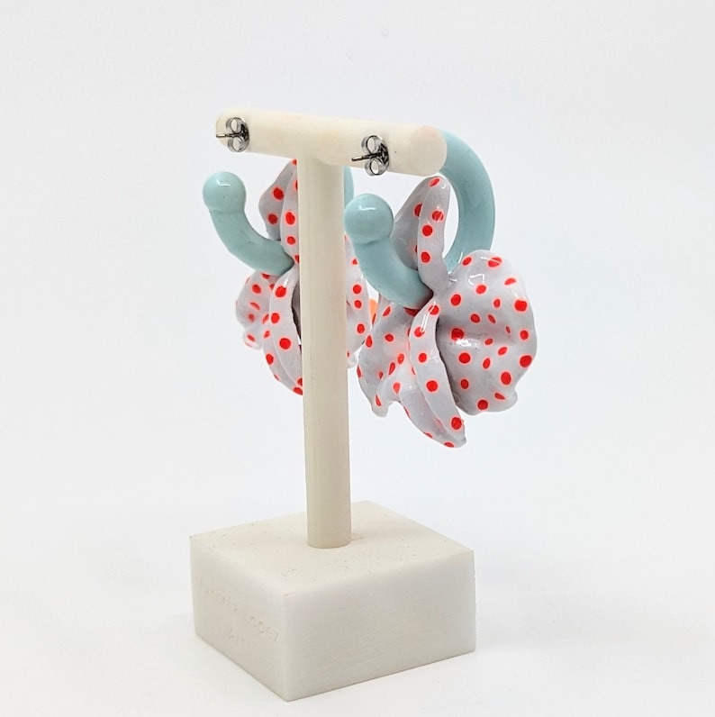 May include: A pair of hoop earrings with a white and red polka dot design. The earrings are made of a light blue material and have a silver hook closure.