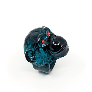 May include: A teal blue and black monkey head ring with red eyes. The ring is made of resin and is a statement piece.