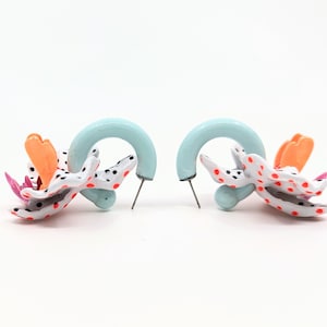 May include: A pair of earrings with a blue hoop and a white, orange, and pink flower design. The flower has black polka dots.