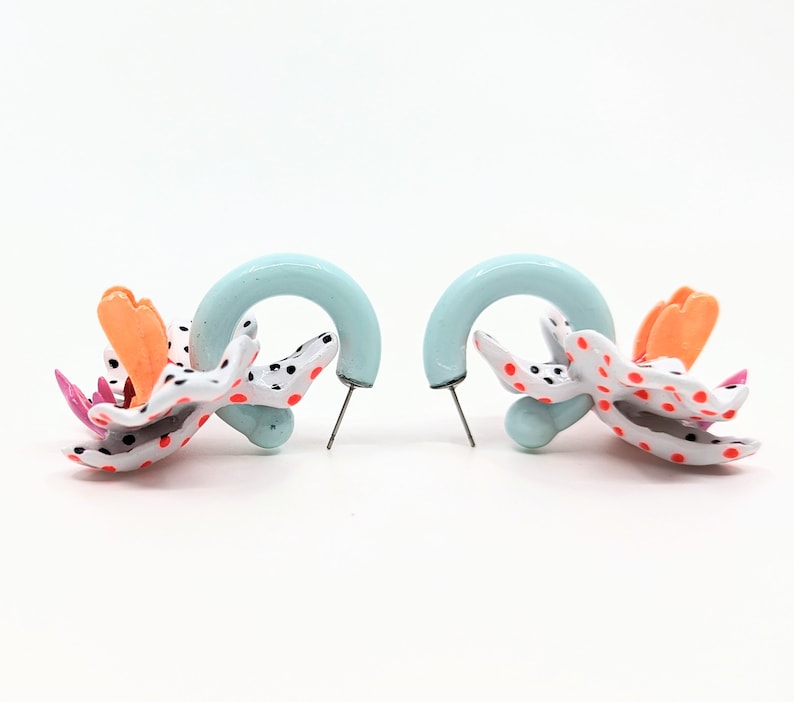 May include: A pair of earrings with a blue hoop and a white, orange, and pink flower design. The flower has black polka dots.