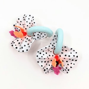 May include: A pair of blue and white enamel earrings shaped like orchids with black polka dots. The earrings have a light blue loop for hanging.