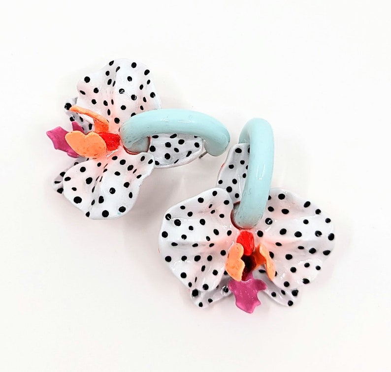 May include: A pair of blue and white enamel earrings shaped like orchids with black polka dots. The earrings have a light blue loop for hanging.