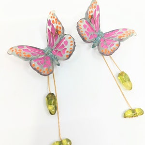 May include: A pair of butterfly earrings with pink, orange, and blue accents. Each butterfly has a gold chain with a green chrysalis and a green caterpillar dangling from it.