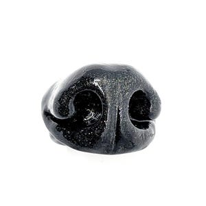 Könnte beinhalten: Eine schwarze, glänzende, dreidimensionale Tierskulptur in Form einer Nase mit einer texturierten, glitzernden Oberfläche. Das Objekt zeigt zwei ausgeprägte, abgerundete Nasenlöcher, die durch einen Mittelsteg getrennt sind und eine realistische Form bilden.
