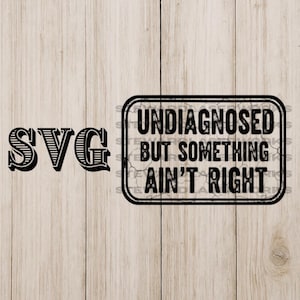 Könnte beinhalten: Schwarzes SVG-Design mit dem Text "SVG" auf der linken Seite und einem rechteckigen Schild auf der rechten Seite. Das Schild lautet "UNDIAGNOSED BUT SOMETHING AIN'T RIGHT" in schwarzem Text. Der Hintergrund ist eine helle Holzmaserung.