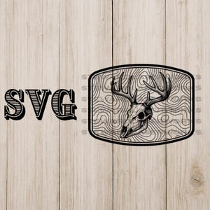 May include: Black and white SVG design featuring a deer skull with antlers inside a rectangular frame. The frame has a wood grain pattern. The word "SVG" is printed in large, bold letters to the left of the frame.