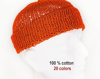 Könnte beinhalten: Eine leuchtend orangefarbene Strickmütze mit gerolltem Rand und einem offenen, strukturierten Strickmuster. Der Text 100 % cotton und 20 colors ist unter der Mütze zu sehen. Die Mütze wird auf einem weißen Schaufensterpuppenkopf vor weißem Hintergrund gezeigt.