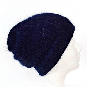 Könnte beinhalten: Eine marineblaue Strickmütze. Die Mütze ist aus einem weichen, strukturierten Material gefertigt und hat eine leicht lockere Passform. Die Mütze wird auf einem weißen Schaufensterkopf vor weißem Hintergrund gezeigt. Die Mütze ist einfarbig ohne sichtbare Muster.