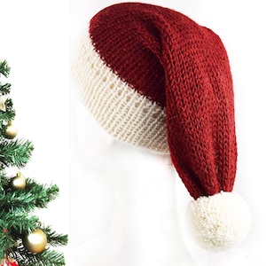 Könnte beinhalten: Eine gestrickte Weihnachtsmütze mit weißer Basis und rotem Oberteil. Die Mütze hat einen weißen Bommel am Ende. Die Mütze befindet sich neben einem Weihnachtsbaum mit goldenen Ornamenten.