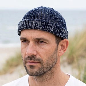 Könnte beinhalten: Eine dunkelblaue Strickmütze mit gesprenkelter weißer Textur und einem dicken, umgeschlagenen Rand. Die Mütze hat eine eng gerippte Struktur und sitzt fest auf dem Kopf. Der Text unten lautet: Echtes Produkt. KI-generiertes Bild zur Präsentation.