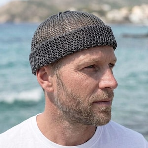 May include: A dark gray, close-fitting beanie cap with a distinct, open-knit, chain-link texture and a wide, folded cuff. The hat features a rounded crown and a consistent, uniform weave pattern throughout the entire structure of the headwear.