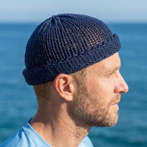 Könnte beinhalten: Eine dunkelblaue Strickmütze mit gerolltem Rand. Die Mütze zeichnet sich durch eine strukturierte Strickweise mit offenen Maschen aus, die eng am Kopf anliegt und ein schlichtes, funktionales Design bietet, das den Kopf ohne Details bedeckt.