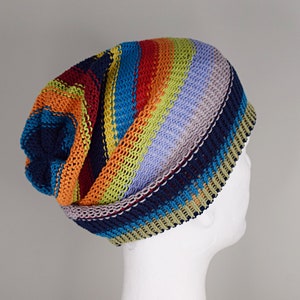 May include: A slouchy knit beanie featuring horizontal stripes in vibrant colors including navy blue, orange, lime green, and light purple. The hat is constructed with a textured, ribbed knit pattern and has a folded brim edge.