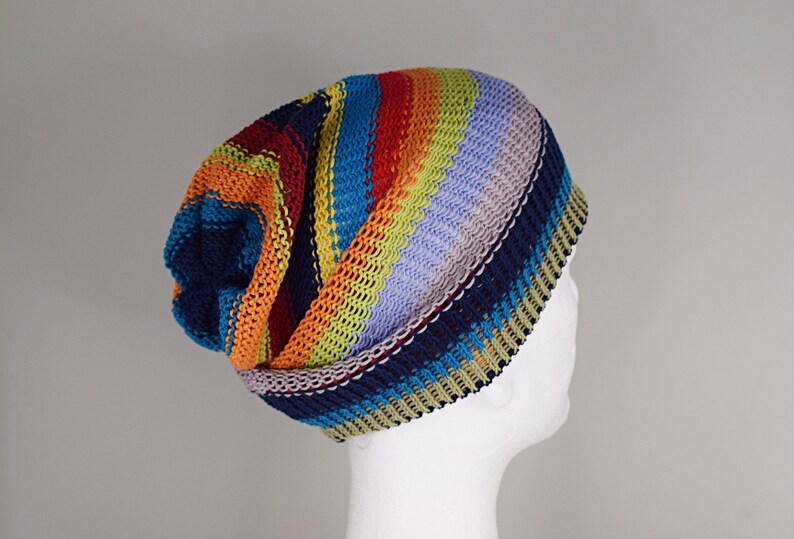 May include: A slouchy knit beanie featuring horizontal stripes in vibrant colors including navy blue, orange, lime green, and light purple. The hat is constructed with a textured, ribbed knit pattern and has a folded brim edge.