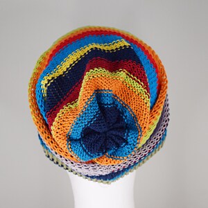 May include: A knit beanie featuring horizontal stripes in vibrant colors including navy blue, bright orange, lime green, turquoise, and light purple. The hat has a gathered crown design with a solid navy blue center point and a textured knit pattern.