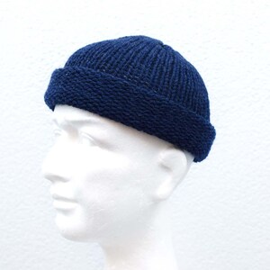 May include: A dark navy blue knit beanie cap with a thick, folded brim. The hat features a vertical ribbed texture on the crown and a distinct, tighter knit pattern on the cuff, providing a snug fit around the head with a classic, rounded silhouette.