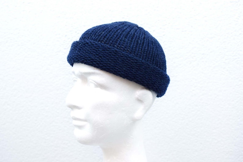 May include: A dark navy blue knit beanie cap with a thick, folded brim. The hat features a vertical ribbed texture on the crown and a distinct, tighter knit pattern on the cuff, providing a snug fit around the head with a classic, rounded silhouette.
