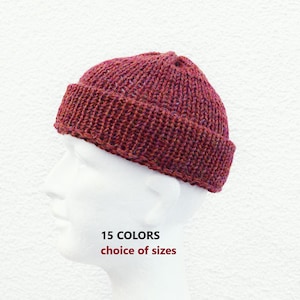 Könnte beinhalten: Eine gestrickte bordeauxfarbene Beanie-Mütze mit umgeschlagenem Rand, präsentiert auf einem weißen Schaufensterkopf. Die Mütze ist aus einem strukturierten Garn gefertigt. Der Text auf dem Bild lautet "15 FARBEN Auswahl an Größen."