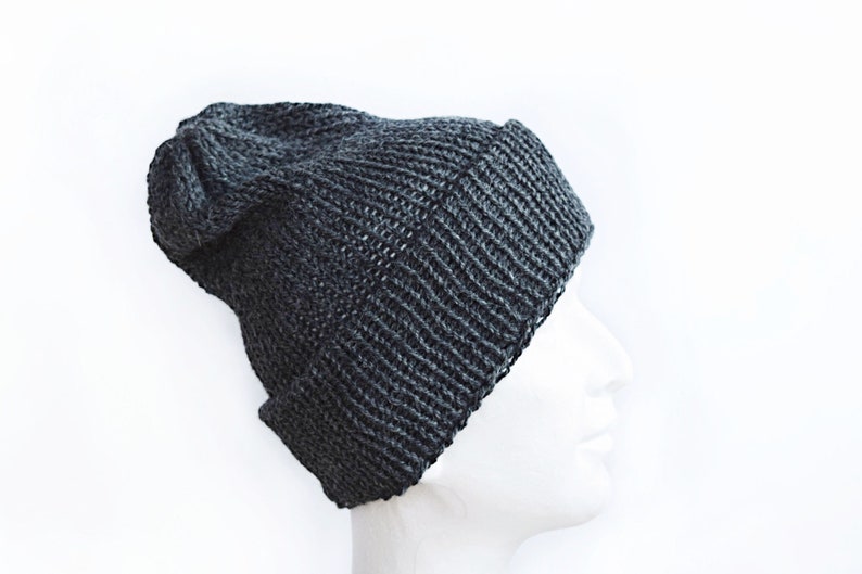 K&ouml;nnte beinhalten: Eine dunkel anthrazitfarbene Strickm&uuml;tze mit geripptem Umschlag und einer leicht locker sitzenden Krone. Die M&uuml;tze ist aus dickem Garn mit einem sichtbaren Strickmuster gefertigt und verf&uuml;gt &uuml;ber einen umgeschlagenen Rand.