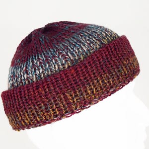 Pu&ograve; includere: Un berretto in maglia con bordo risvoltato e un motivo a filato variegato. Il cappello presenta una ricca tavolozza di colori bordeaux profondo, rosso scuro e sottili sfumature di blu e oro nella struttura in lana lavorata a mano.