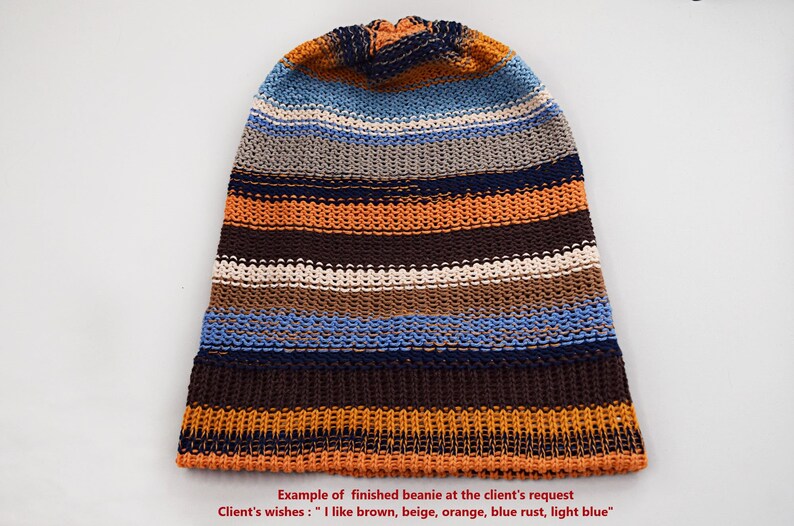 May include: A knit beanie featuring horizontal stripes in shades of brown, beige, orange, light blue, and dark blue. The text at the bottom reads: Example of finished beanie at the client's request. Client's wishes : "I like brown, beige, orange, blue rust, light blue".