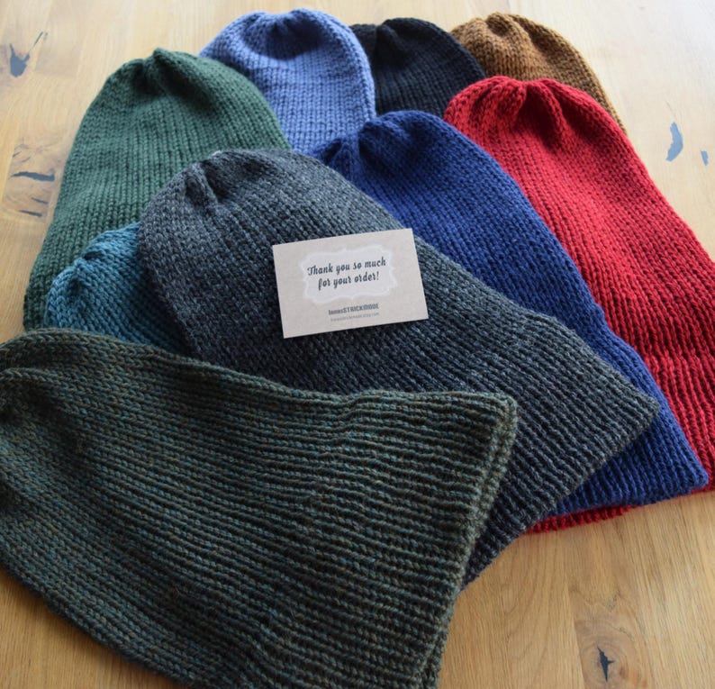 K&ouml;nnte beinhalten: Eine Sammlung von gestrickten M&uuml;tzen in verschiedenen Farben, darunter Dunkelgr&uuml;n, Anthrazit, Blau, Schwarz, Braun und Rot. Auf der anthrazitfarbenen M&uuml;tze liegt eine kleine rechteckige beigefarbene Karte mit dem Text Thank you so much for your order!