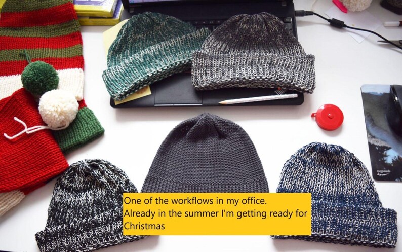 May include: A collection of six knitted beanies in various colors including green, grey, black, and blue, alongside a red and green striped stocking with two pom-poms. The image includes the text: One of the workflows in my office. Already in the summer I'm getting ready for Christmas.