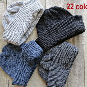 May include: Four knitted beanies in light gray, black, dark blue, and charcoal gray. Each hat features a thick ribbed cuff and a textured knit pattern. The text 22 colors is printed in red in the upper right corner of the image.