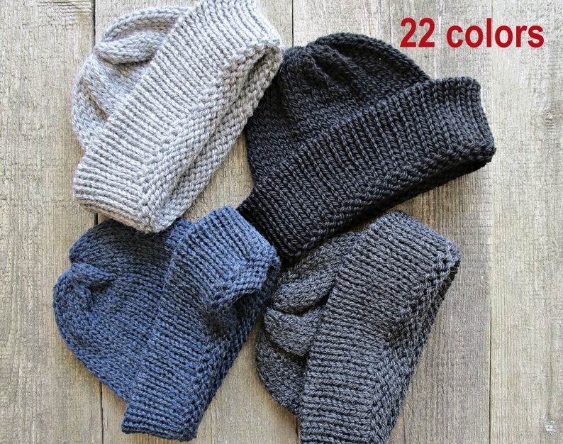 May include: Four knitted beanies in light gray, black, dark blue, and charcoal gray. Each hat features a thick ribbed cuff and a textured knit pattern. The text 22 colors is printed in red in the upper right corner of the image.