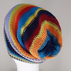 May include: A slouchy knit beanie featuring horizontal stripes in vibrant colors including navy blue, bright orange, red, turquoise, lime green, and light lavender. The hat is constructed with a textured garter stitch pattern throughout.